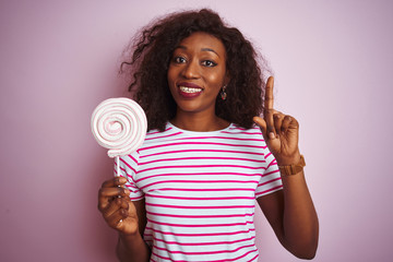 Young african american woman eating sweet candy standing over isolated pink background surprised with an idea or question pointing finger with happy face, number one