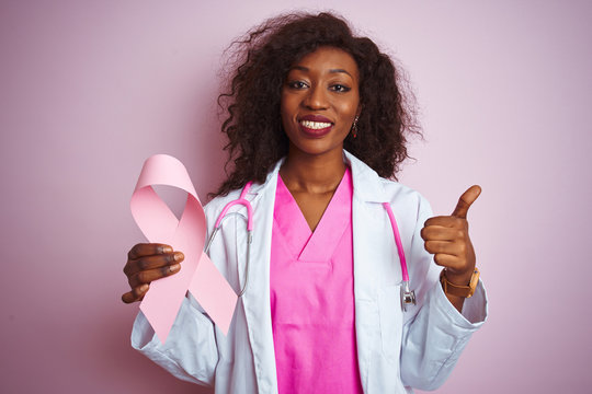 Young african american doctor woman holding cancer ribbon over isolated pink background happy with big smile doing ok sign, thumb up with fingers, excellent sign