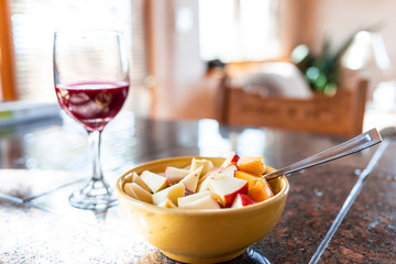 Closeup of one bowl with apple and peach slices on porridge with bokeh background of red wine glass on kitchen counter or restaurant