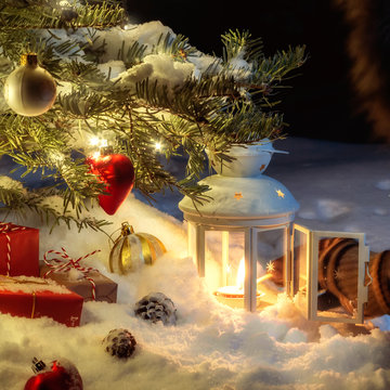 Christmas composition - a tree in the snow, gifts, decoration and a hand lighting a lantern with a match