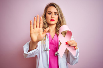 Young beautiful doctor woman holding cancer ribbon over pink isolated background with open hand...
