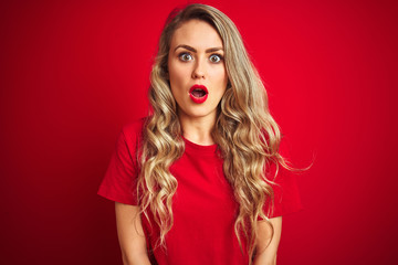Young beautiful woman wearing basic t-shirt standing over red isolated background afraid and shocked with surprise expression, fear and excited face.