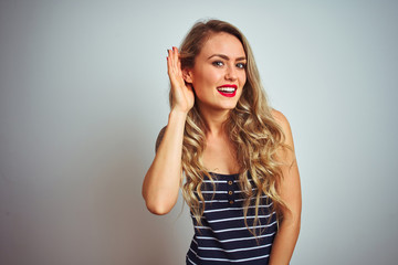 Fototapeta premium Young beautiful woman wearing stripes t-shirt standing over white isolated background smiling with hand over ear listening an hearing to rumor or gossip. Deafness concept.