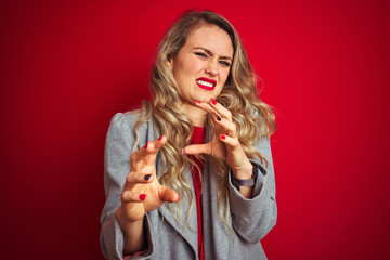 Young beautiful business woman wearing elegant jacket standing over red isolated background disgusted expression, displeased and fearful doing disgust face because aversion reaction. 