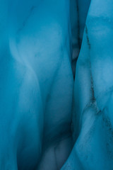Deep within an ice cave looking in with deep blue color to the curvy ice walls.
