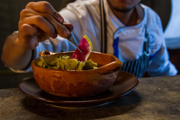 Restaurant chef garnishing traditional mexican chilaquiles on a mud plate