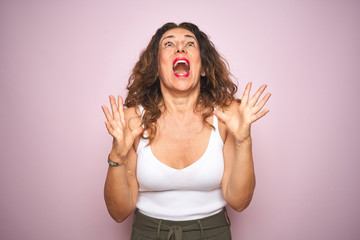 Middle age senior woman standing over pink isolated background crazy and mad shouting and yelling with aggressive expression and arms raised. Frustration concept.