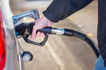 A man in a blue jeans and black coat holding pump filling gasoline. Pumping petrol into the tank. A...