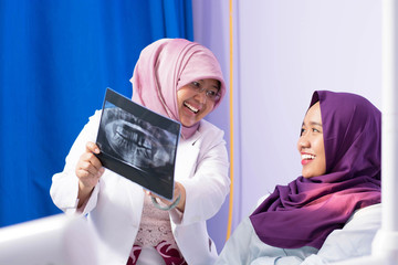 Happy Islam Hijab female dentist doctor explaining radiology x ray result to Muslim patient on dentist chair in dental clinic