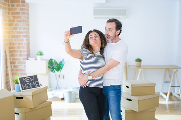 Obraz na płótnie Canvas Middle age senior romantic couple taking a selfie picture with smartphone smiling happy for moving to a new house, making apartment memories