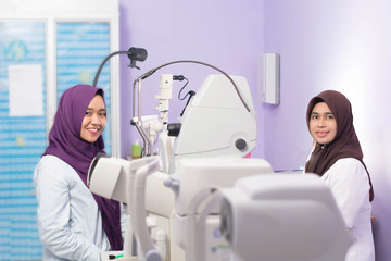 two hijabi female Muslim smiling at camera with ophthalmologist instruments tools in eye hospital clinic