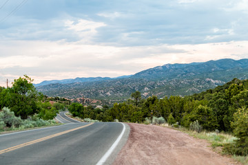 Sunset on Bishops Lodge Road in Santa Fe, New Mexico with pink sunlight on green plants and road to...