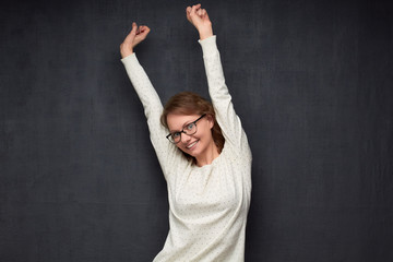 Portrait of happy girl with glasses raising hands while dancing