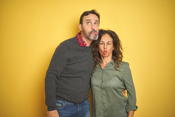 Beautiful middle age couple over isolated yellow background making fish face with lips, crazy and comical gesture. Funny expression.