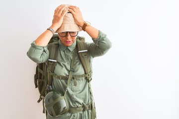 Middle age hiker woman wearing backpack canteen hat glasses over isolated white background suffering from headache desperate and stressed because pain and migraine. Hands on head.