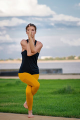 Young beautiful woman practicing yoga with cloudy sky in the background. Wellness concept. Calmness and relax, woman happiness. Yoga is the best holistic workout. Mental and physical health. 