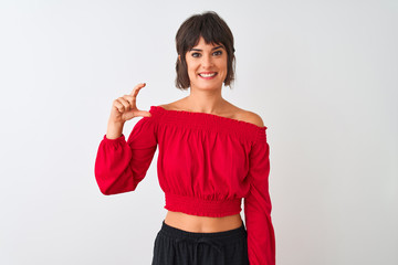 Young beautiful woman wearing red summer t-shirt standing over isolated white background smiling and confident gesturing with hand doing small size sign with fingers looking and the camera. 