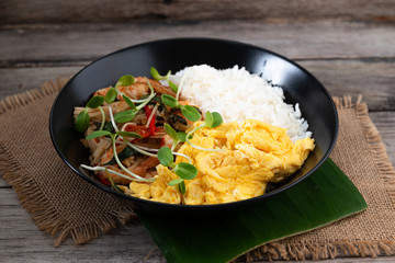 Rice topped with stir-fried shrimp and basil, and fried eggs in white dish.