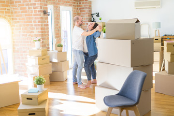 Young couple dancing around cardboard boxes at new home, celebrating smiling very happy new house