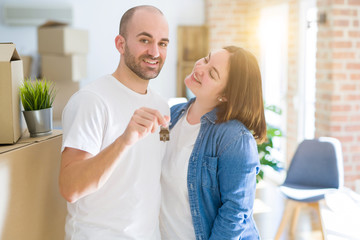 Fototapeta premium Young couple smiling very happy showing keys of new home, moving and buying new apartmet concept