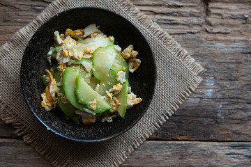 Fresh chayote fruits (Sechium edulis) stir fried with egg and garlic in bowl on wood background