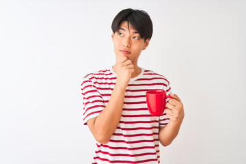 Young chinese man drinking a cup of coffee standing over isolated white background serious face...