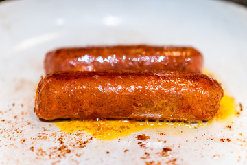 Closeup of two vegan meat sausages cooking on ceramic nonstick frying pan