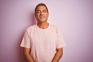 Handsome middle age man wearing t-shirt standing over isolated pink background with serious expression on face. Simple and natural looking at the camera.