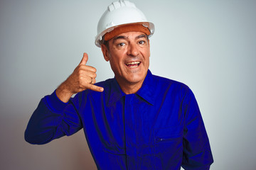 Handsome middle age worker man wearing uniform and helmet over isolated white background smiling doing phone gesture with hand and fingers like talking on the telephone. Communicating concepts.