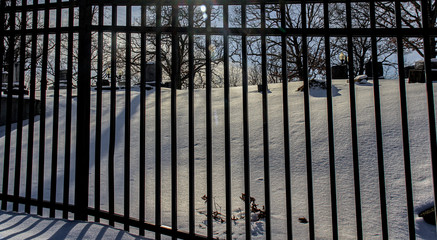 Black rod iron fence. Look through the fence into a snow covered graveyard.