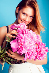 young pretty blond girl posing on blue background, fashion style lady holding bouquet of pink piony flowers , lifestyle people concept