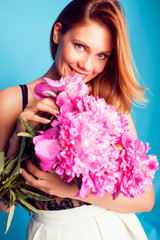 Naklejka premium young pretty blond girl posing on blue background, fashion style lady holding bouquet of pink piony flowers , lifestyle people concept