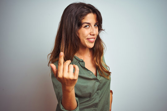 Young beautiful woman wearing green shirt standing over grey isolated background Beckoning come here gesture with hand inviting welcoming happy and smiling