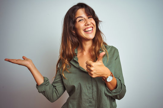 Young beautiful woman wearing green shirt standing over grey isolated background Showing palm hand and doing ok gesture with thumbs up, smiling happy and cheerful