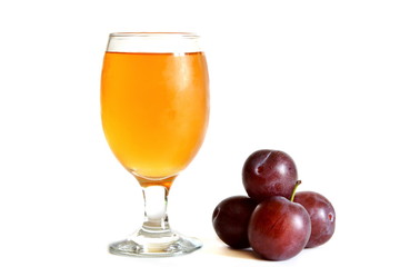 Misted glass goblet with light juice next heap of ripe plum on white background. Isolated
