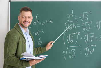 Handsome math teacher near blackboard in classroom - obrazy, fototapety, plakaty