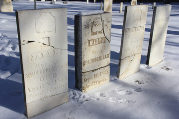 100 yr. old tomb stones in a snow covored grave yard. Names are fading and stones are cracking.