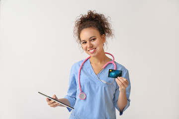 African-American doctor with credit card and tablet computer on light background