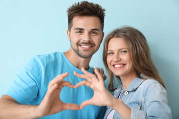 Young couple holding hands in shape of heart on color background