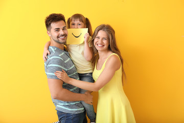 Portrait of happy family with drawn smile on sheet of paper against color background