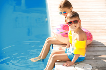 Cute little children sitting near swimming pool