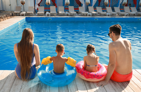 Young Family Sitting Near Swimming Pool, Back View