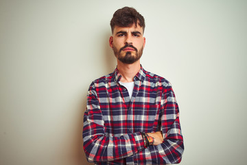 Young man wearing casual shirt standing over isolated white background skeptic and nervous, disapproving expression on face with crossed arms. Negative person.