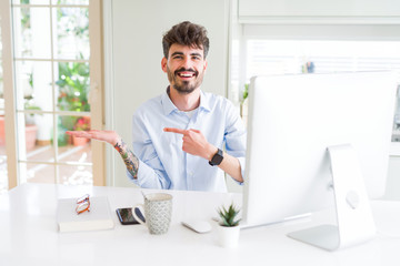 Young business man working using computer amazed and smiling to the camera while presenting with hand and pointing with finger.