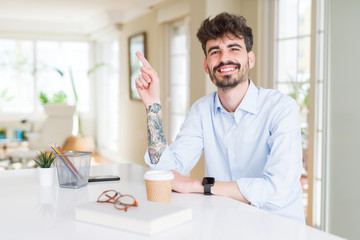 Young business man working with a big smile on face, pointing with hand and finger to the side looking at the camera.