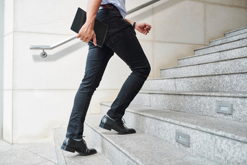 Cropped image of entrepreneur in a hurry with digital tablet in hands running up the stairs to...