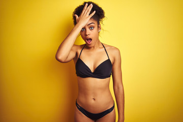 African american woman on vacation wearing bikini standing over isolated yellow background surprised with hand on head for mistake, remember error. Forgot, bad memory concept. - obrazy, fototapety, plakaty