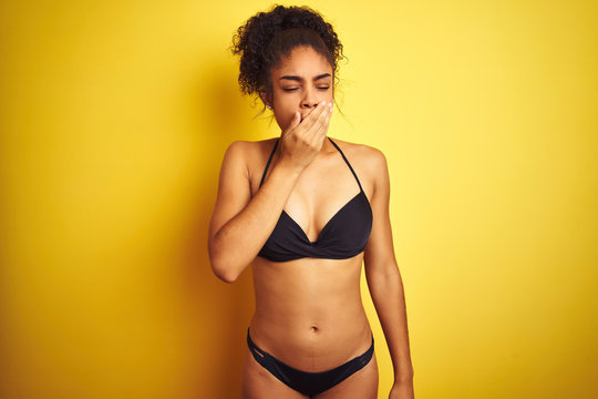 African american woman on vacation wearing bikini standing over isolated yellow background bored yawning tired covering mouth with hand. Restless and sleepiness.