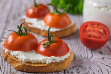 Toasted toast with fresh cottage cheese and tomatoes on a wooden table.