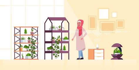 arab woman using automatic watering system controlled by smart speaker voice recognition activated assistant concept modern smart home garden interior flat full length horizontal